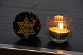 Foto: Während des Vortrags brannte eine Kerze; daneben ein Glas mit aus dem Vernichtungslager Sobibor stammender Erde und Asche, darauf ein Judenstern